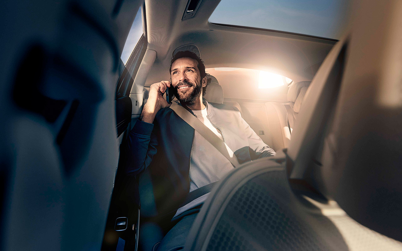 A man sitting in the back seat of a Mercedes-Benz smiles while talking on the phone.
