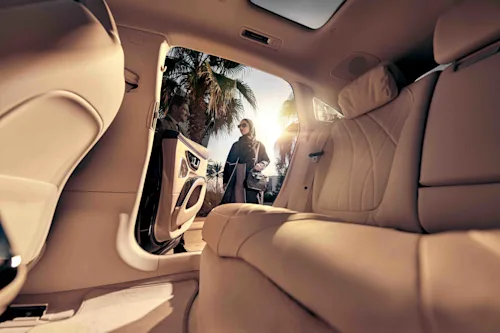 Shot from inside a luxury car as a woman in a headscarf and shades gets into a limousine.