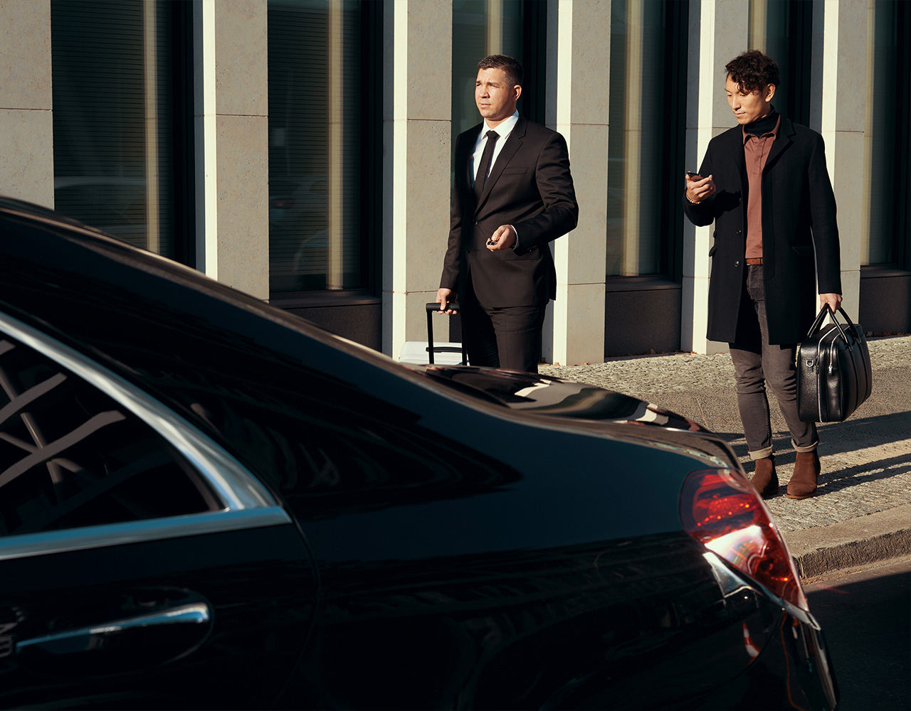 A man checks his phone as he walks toward his vehicle alongside his chauffeur.