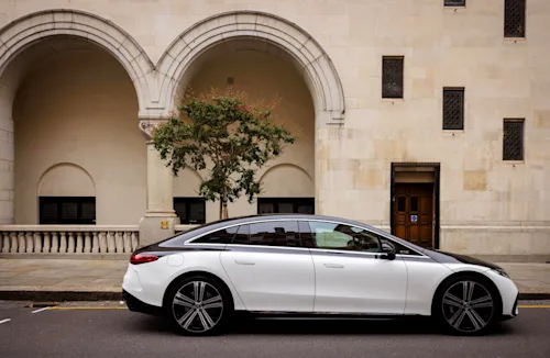Side shot of a Blacklane two-tone Mercedes EQE limo outside an ornate building.