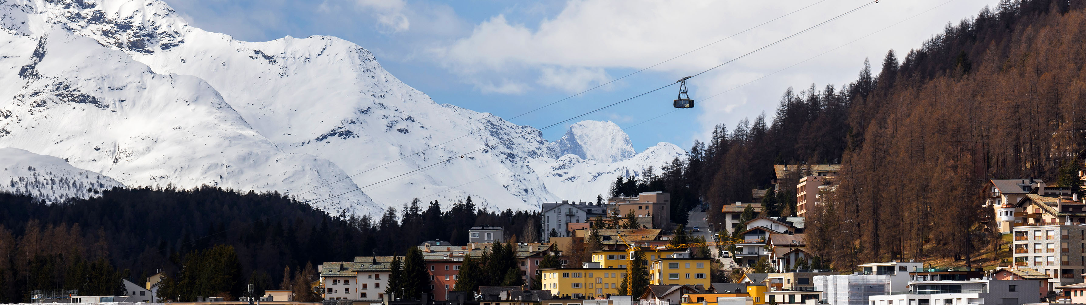 A cable car passes over the colorful houses of Saalbach, with snow capped peaks in the distance.