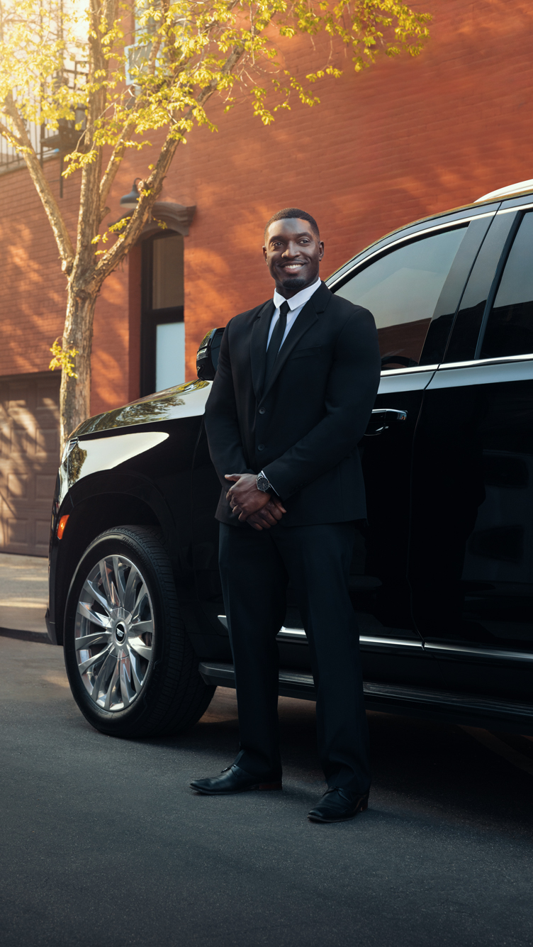 A smiling chauffeur stands next to a black vehicle.