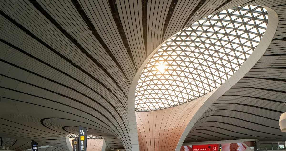 Focus on the soaring roof design of inside the terminal of Beijing Daxing Airport, showing a column and an ornate skylight.