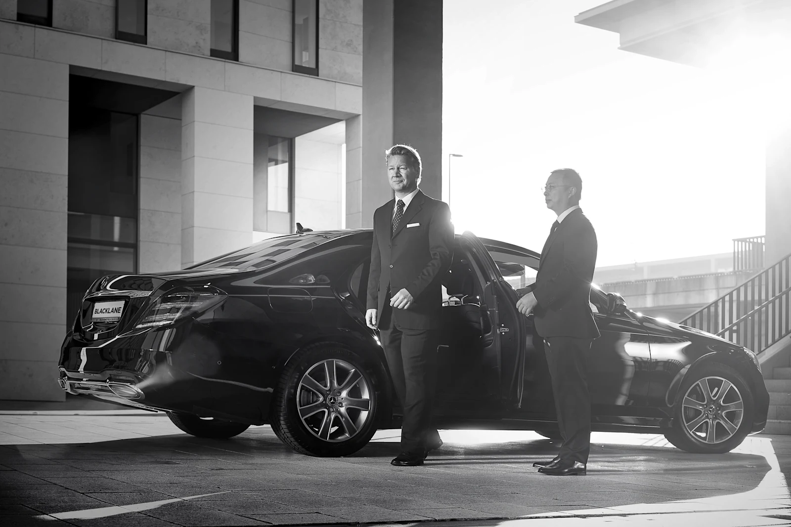 Real Blacklane chauffeur Ben holds the door open for his guest as they exit his Mercedes.