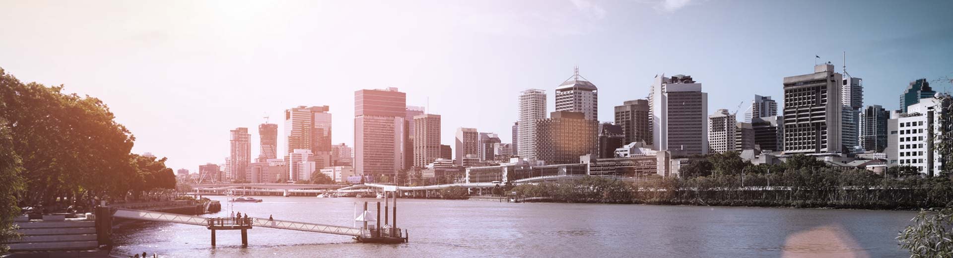 Brisbane Business District à droite, avec des arbres à gauche. Ciel ensoleillé et l'image est prise de l'autre côté de la rivière Brisbane.