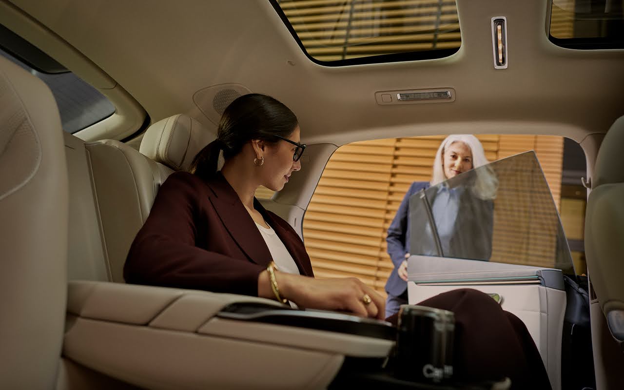 A female business traveler sits in the backseat of a limousine as a chauffeur holds the door open for her.