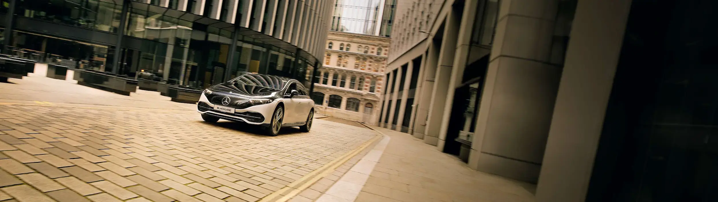 A two-tone electric Mercedes cruises through a city's business district.