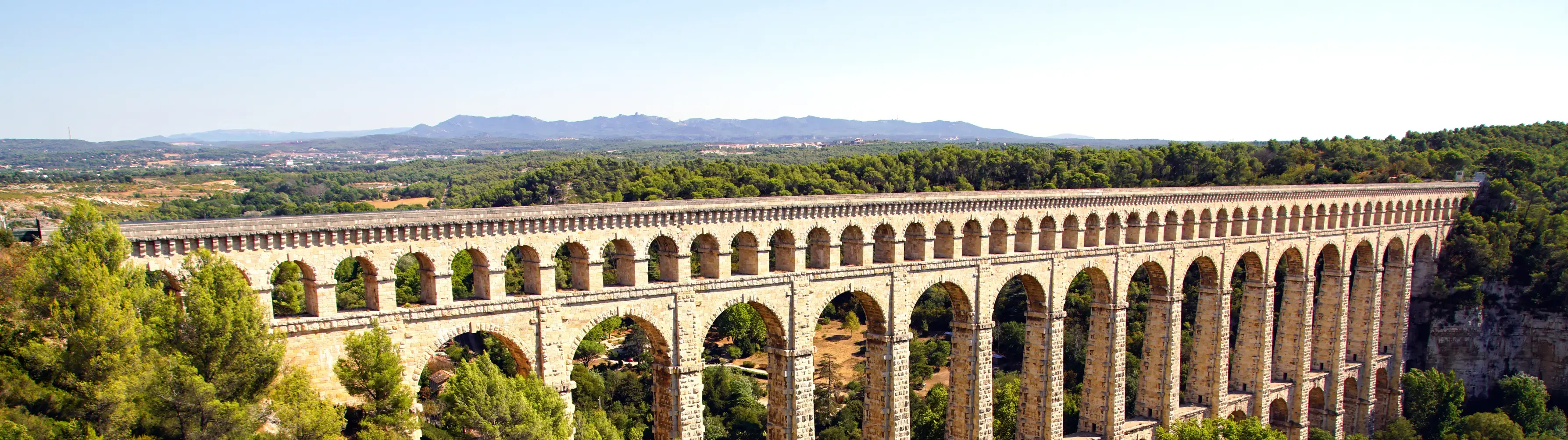 The Pont du Gard aquaduct near Marseille, stretching between dusty brown hills.