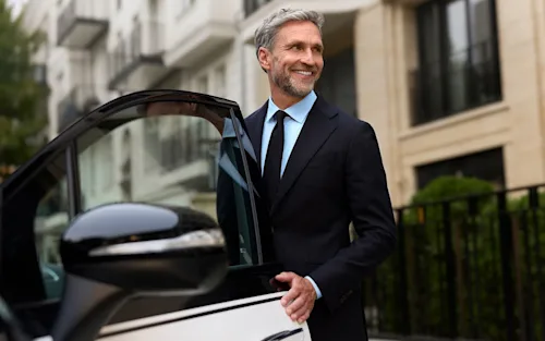 A chauffeur in a suit stands smiling beside a Blacklane limo with the door open.