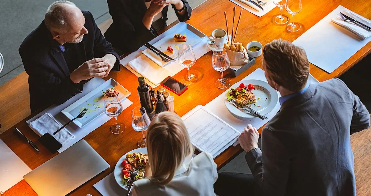 A group of four businesspeople sit down at a private dining table to enjoy a fine dining meal with wine.