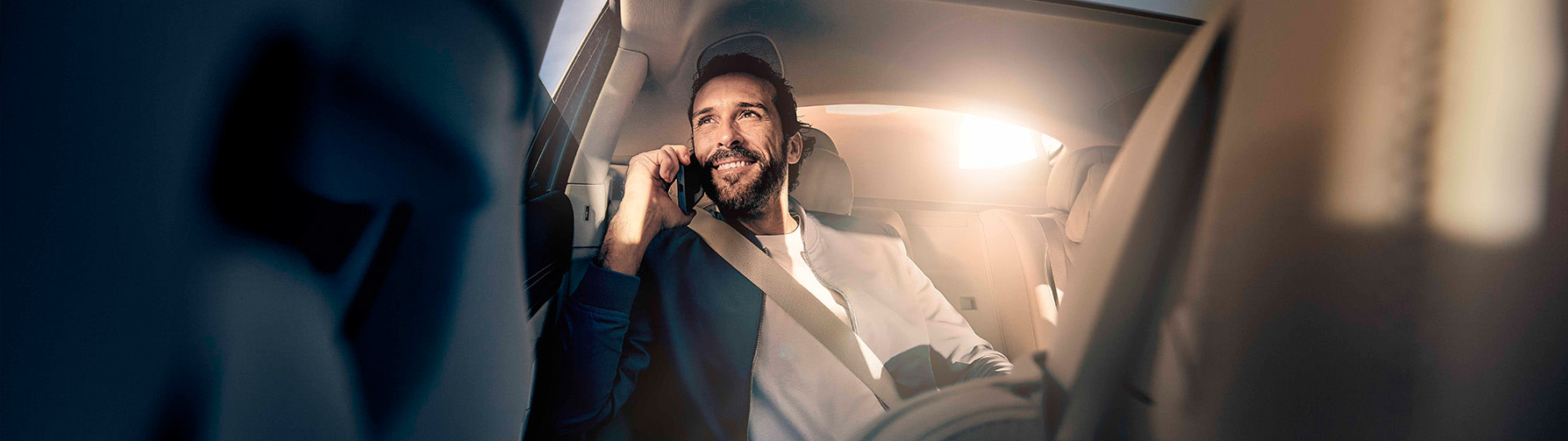 A Blacklane guest smiles while talking on the phone in the back seat of a Mercedes-Benz EQS.