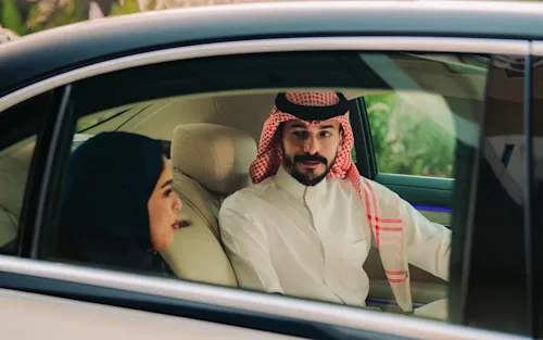 A man in traditional Saudi dress talks to a woman in the backseat of a Mercedes EQS Blacklane limousine.
