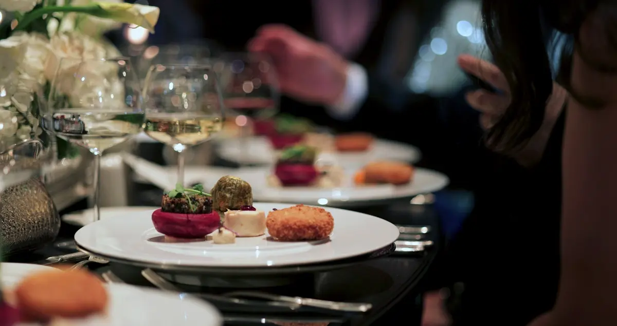 Shot of plates of fine food at a private dining restaurant, with white wine glasses and table dressing in the background.