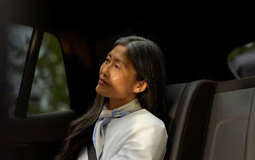 An Asian woman with greying hair and an elegant scarf sits in the back of a Blacklane car service.