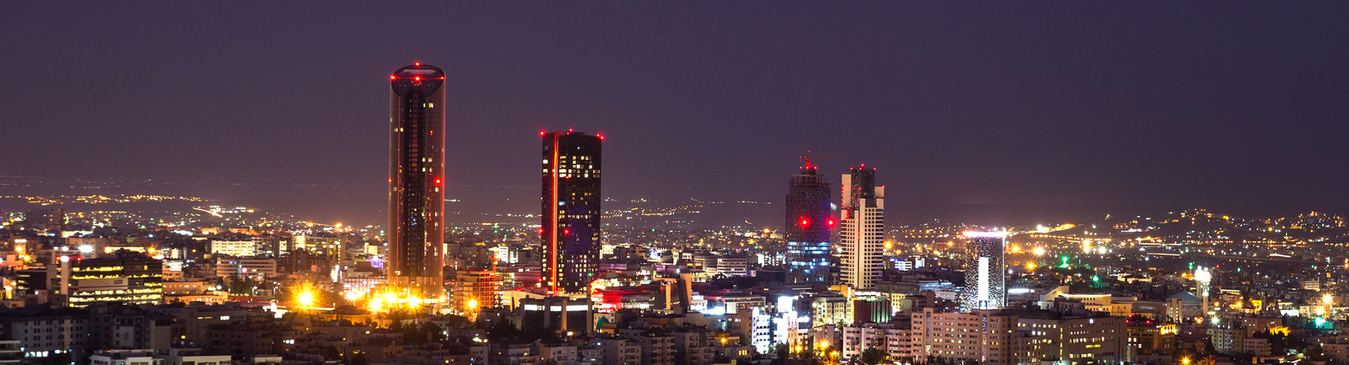 Una noche oscura en Amman mientras tres rascacielos iluminan el área circundante.