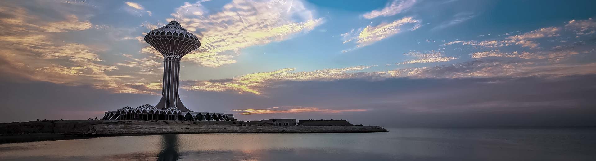 Un énorme bâtiment domine la ligne d'horizon de Dammam au crépuscule, avec un plan d'eau devant lui.