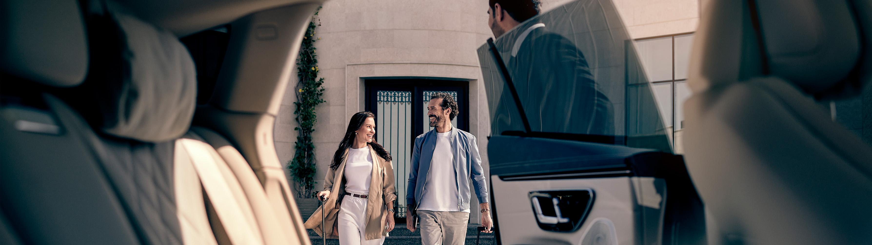 View from inside of 2 guests walking toward backseat, chauffeur holding door