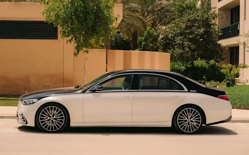 A Blacklane-branded two-tone black and white Mercedes EQE sitting on the street outside a luxury property.