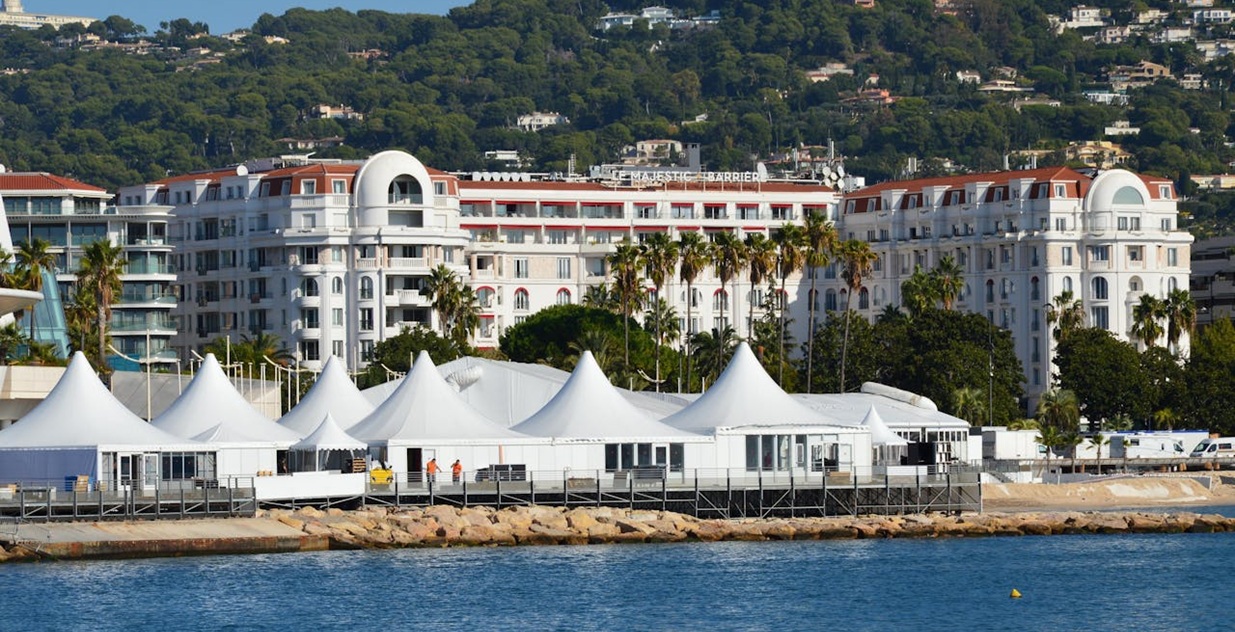 Shot of the Hôtel Barrière Le Majestic in Cannes from the sea, showing some tents on the seafront in the foreground.