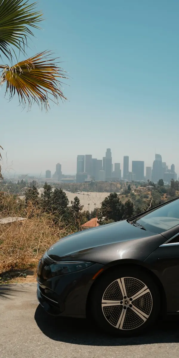 The front of a black Mercedes EQE in the foreground with the skyscrapers of LA in the background.