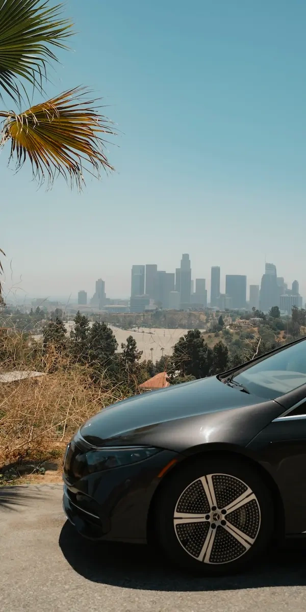 The front of a black Mercedes EQE in the foreground with the skyscrapers of LA in the background.