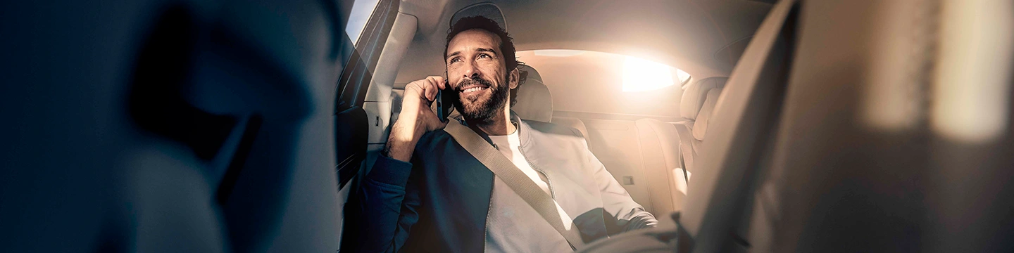 A Blacklane guest in the back seat of a Mercedes-Benz EQS smiles while talking on the phone.