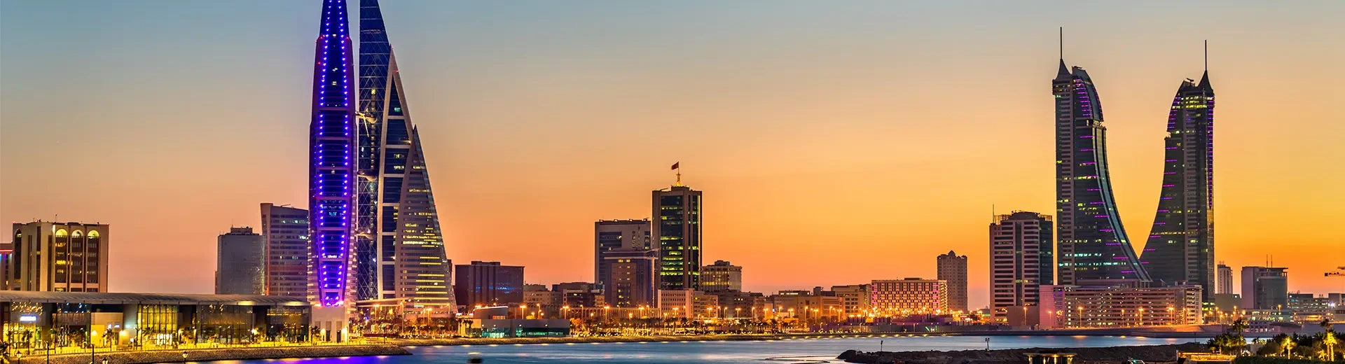 A shot of the Manama cityscape at sunset, showing skyscrapers and the waterfront.