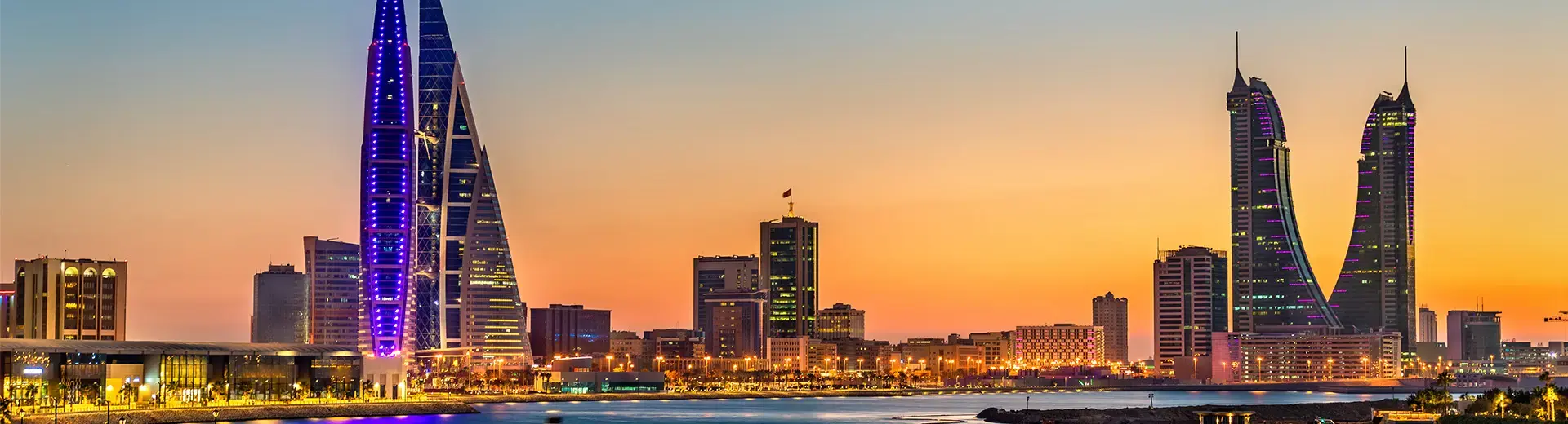 A shot of the Manama cityscape at sunset, showing skyscrapers and the waterfront.