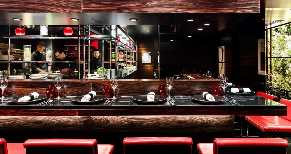 Shot of the open kitchen with bar seats facing it at the Parisian restaurant Atelier Robuchon Etoile, showing chefs at work behind the counter.