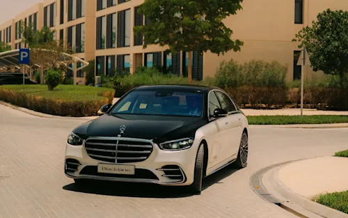 A black-and-white Mercedes EQE from Blacklane turning a corner in a luxury housing estate.
