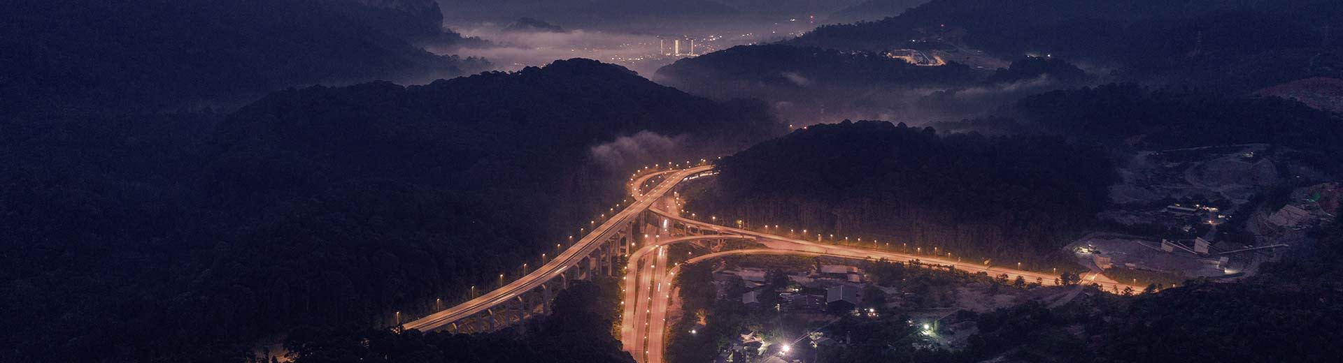 漆黑的山丘环绕着灯火通明的高速公路，远处是拉旺的灯光。
