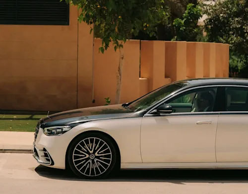 A two-tone Mercedes EQE from Blacklane outside a luxury house in the sun.