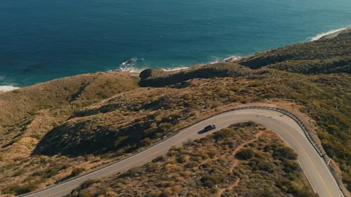 Overhead shot of a car driving around a bend by the sea on the Californian coast.
