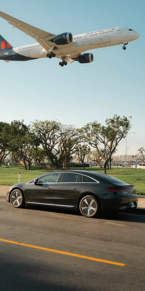 An airplane flies low over a Blacklane Mercedes EQE limo.