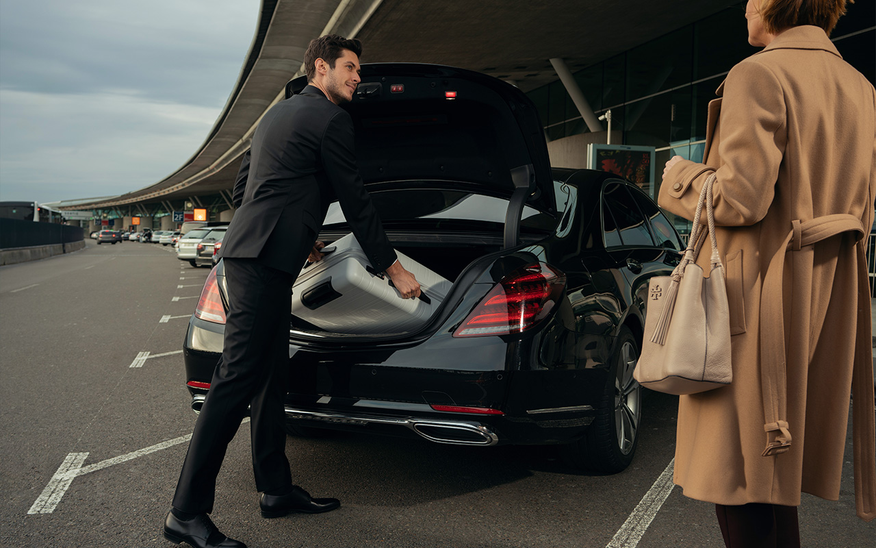 Smiling chauffeur helps put a woman's luggage in the back of his vehicle.
