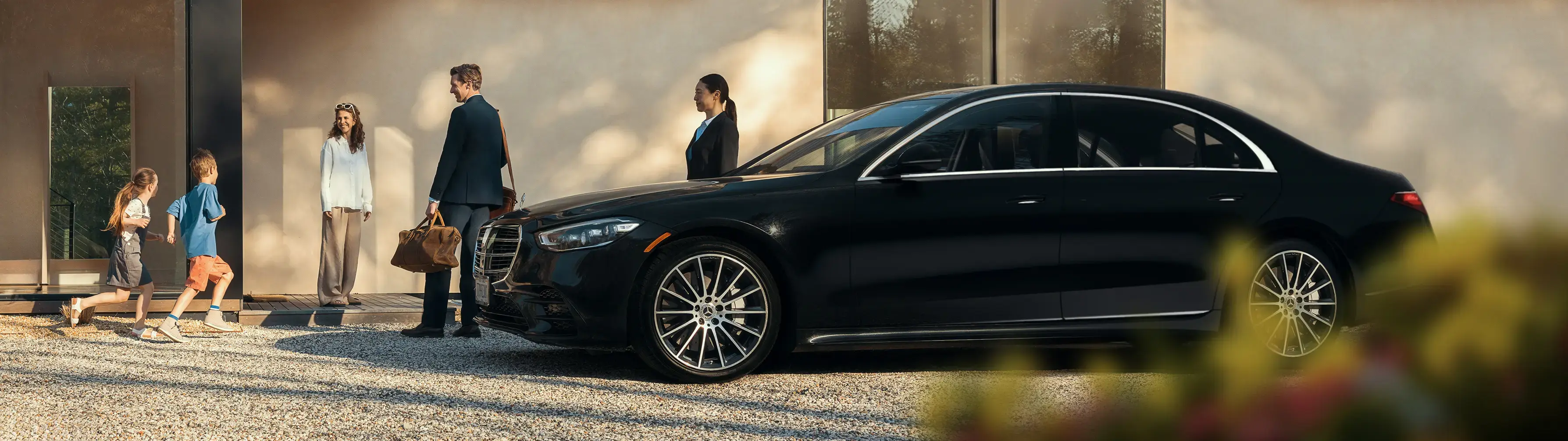 Blacklane-Chauffeur und eine Familie stehen um eine elegante, schwarze Mercedes-Limousine herum.