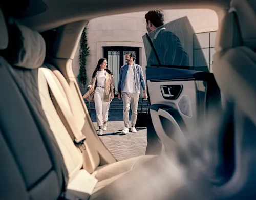 Shot from inside a Blacklane limo at a happy couple walking towards the car, with a chauffeur holding the door open.