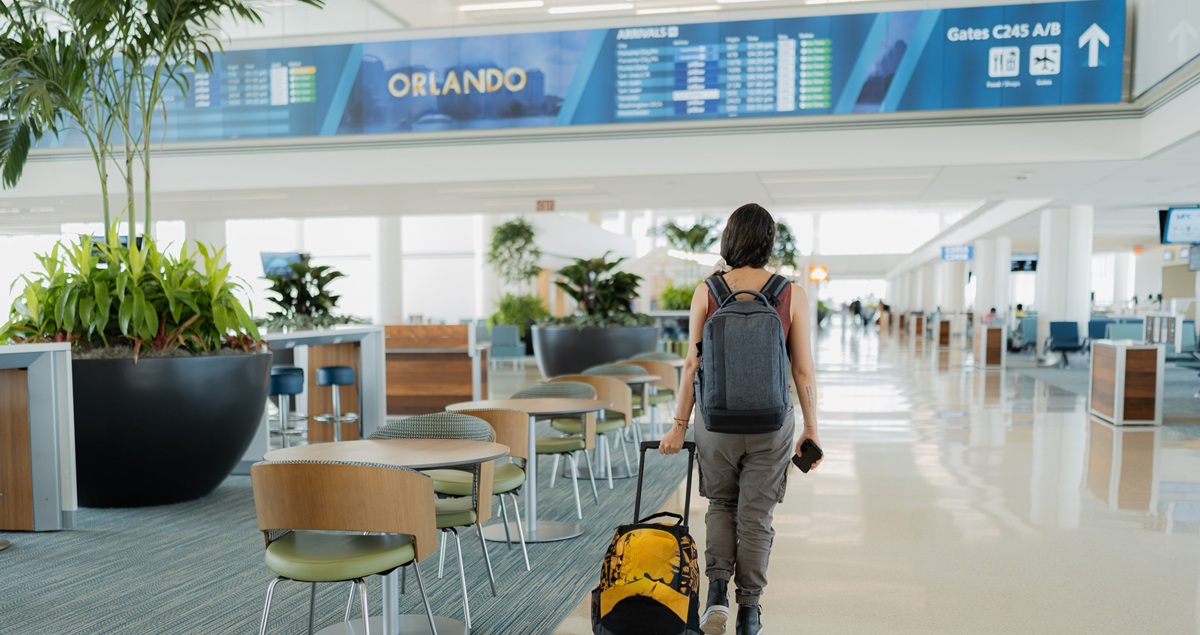 A woman walks through an airport with a bag heading for an Orlando airport lounge.