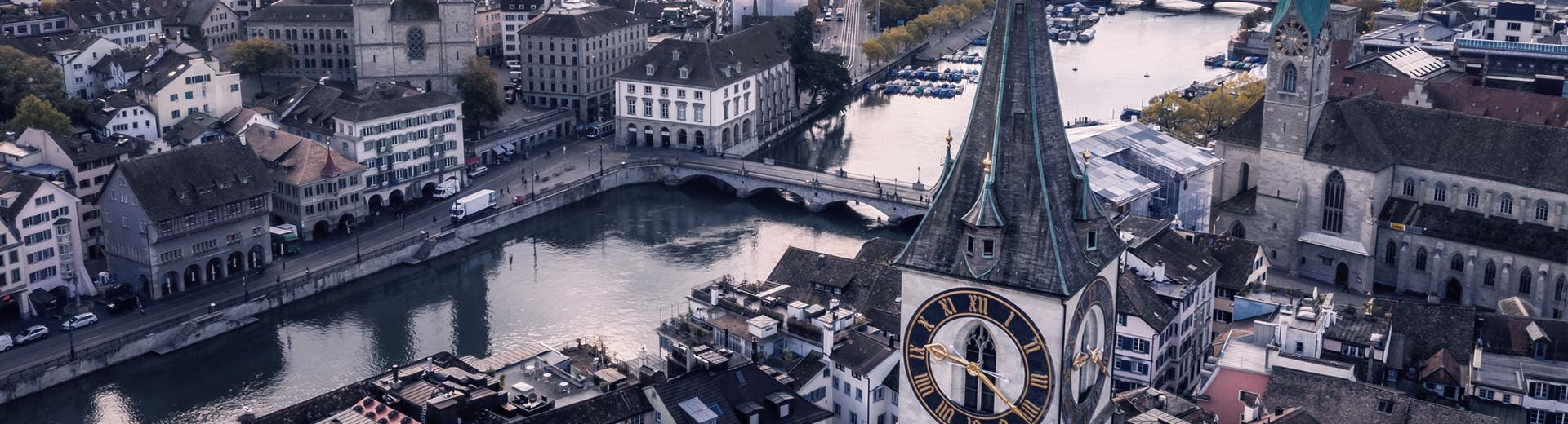 Aerial view of the river Limmat in Zurich at dusk or dawn, with an imposing church before it.