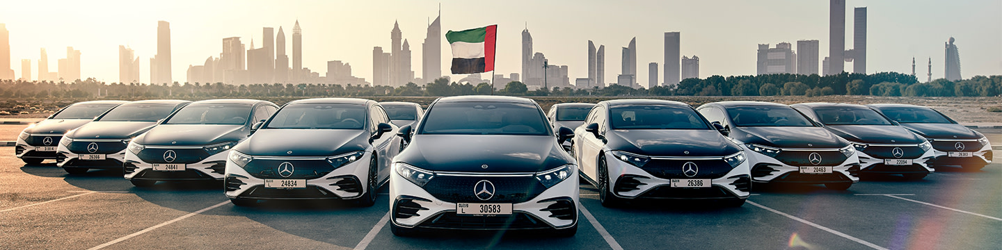 A fleet of Mercedes-Benz EQSes parked in front of the Dubai skyline.