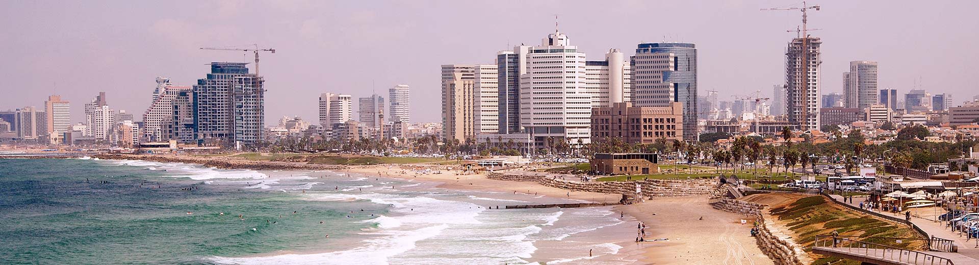 Unter einem wolkigen Tel Aviv -Himmel liegen einige generisch aussehende Wolkenkratzer und Hotels, während sich ein fast leerer Strand im Vordergrund befindet.