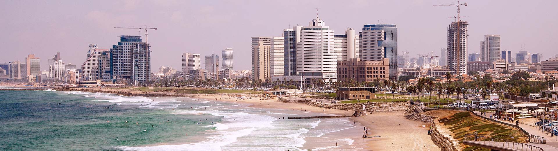 Sous un ciel nuageux de Tel Aviv se trouvent des gratte-ciel et des hôtels génériques, tandis qu'une plage presque vide est au premier plan.