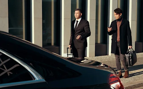 A male passenger walks to his Blacklane airport transfer with his chauffeur carrying his luggage for him.