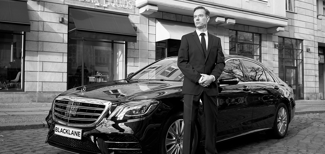 A chauffeur stands outside his vehicle, ready to greet their next guest.