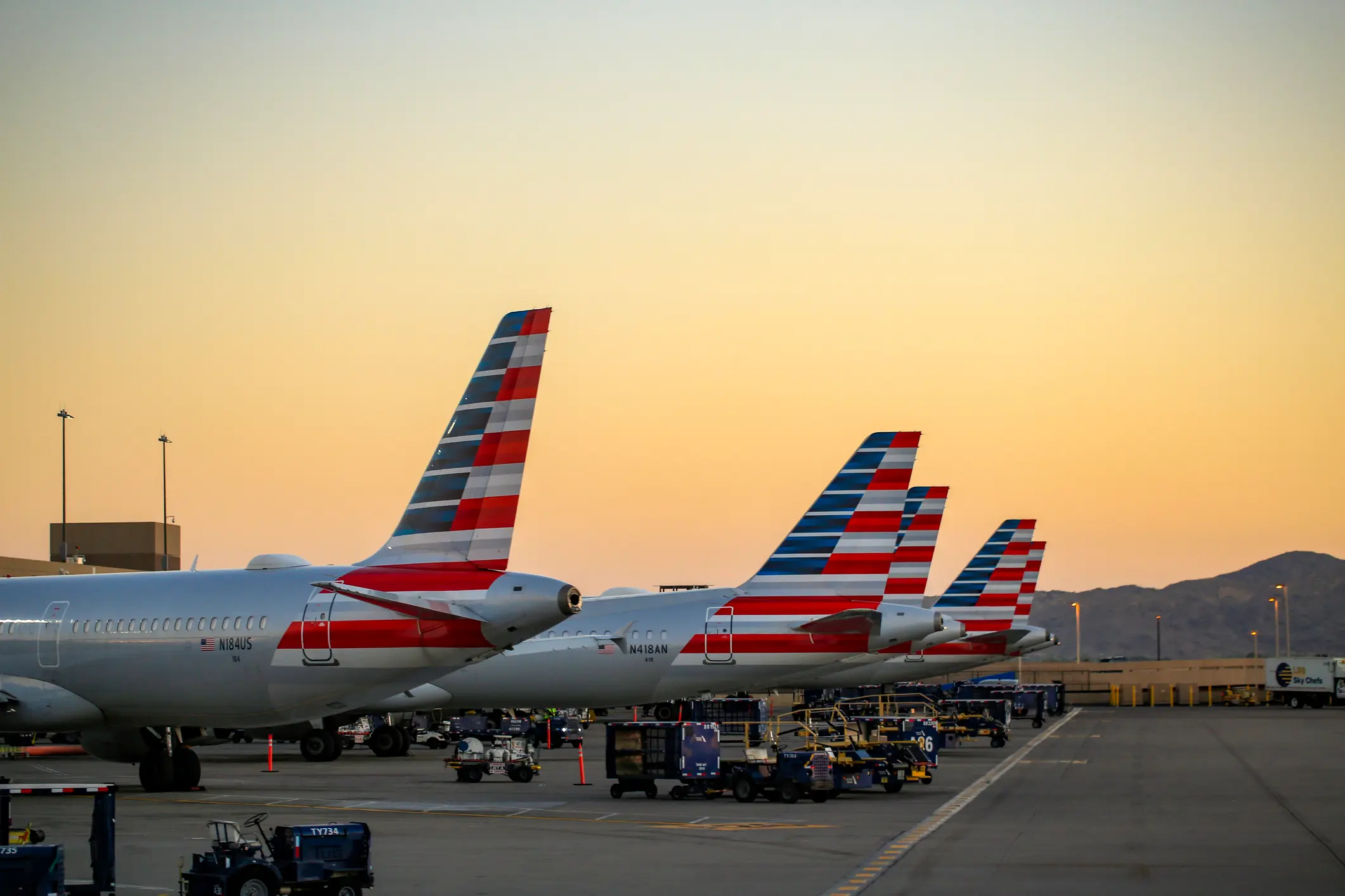 The tailwings of AA planes in American flag livery set against the sunset on the apron at Phoenix Sky Harbour Airport.
