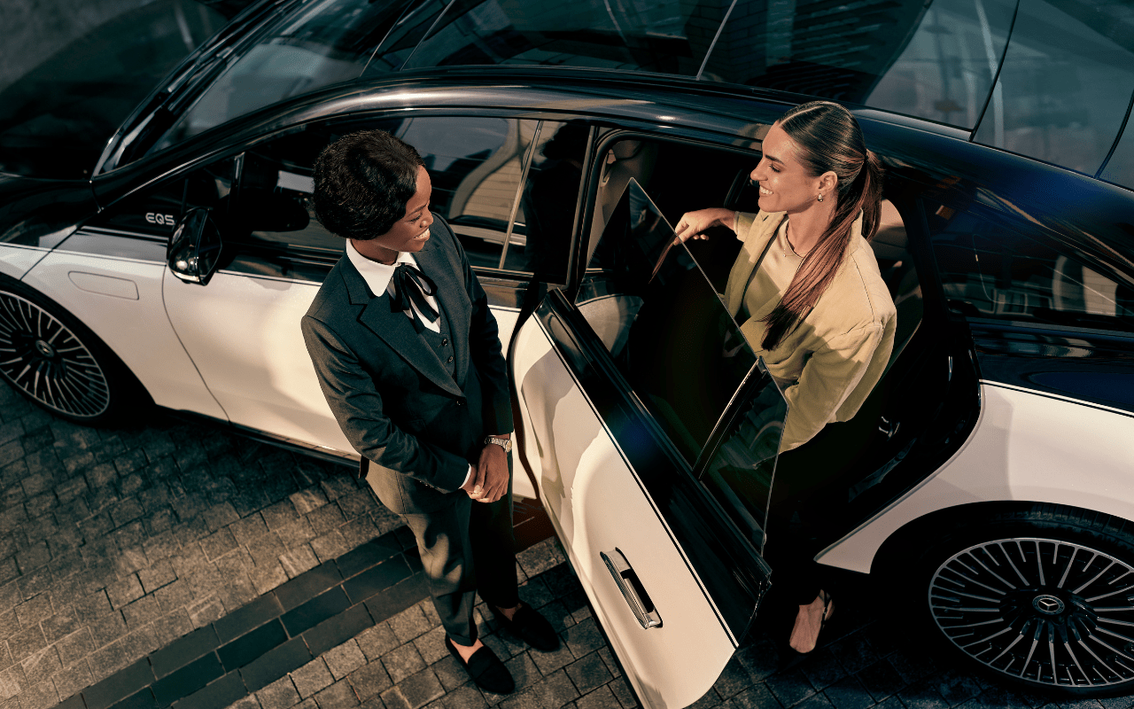 A Blacklane chauffeur holds the car door open for an elegantly-dressed guest.
