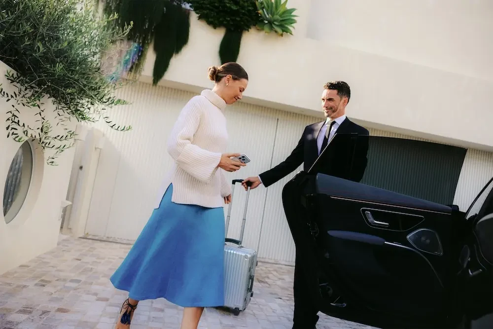 A Blacklane chauffeur holds the car door open for an elegantly-dressed guest.
