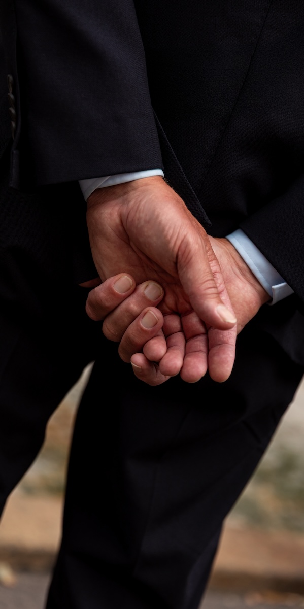Close-up shot of a chauffeur's besuited hands clasped behind their back.