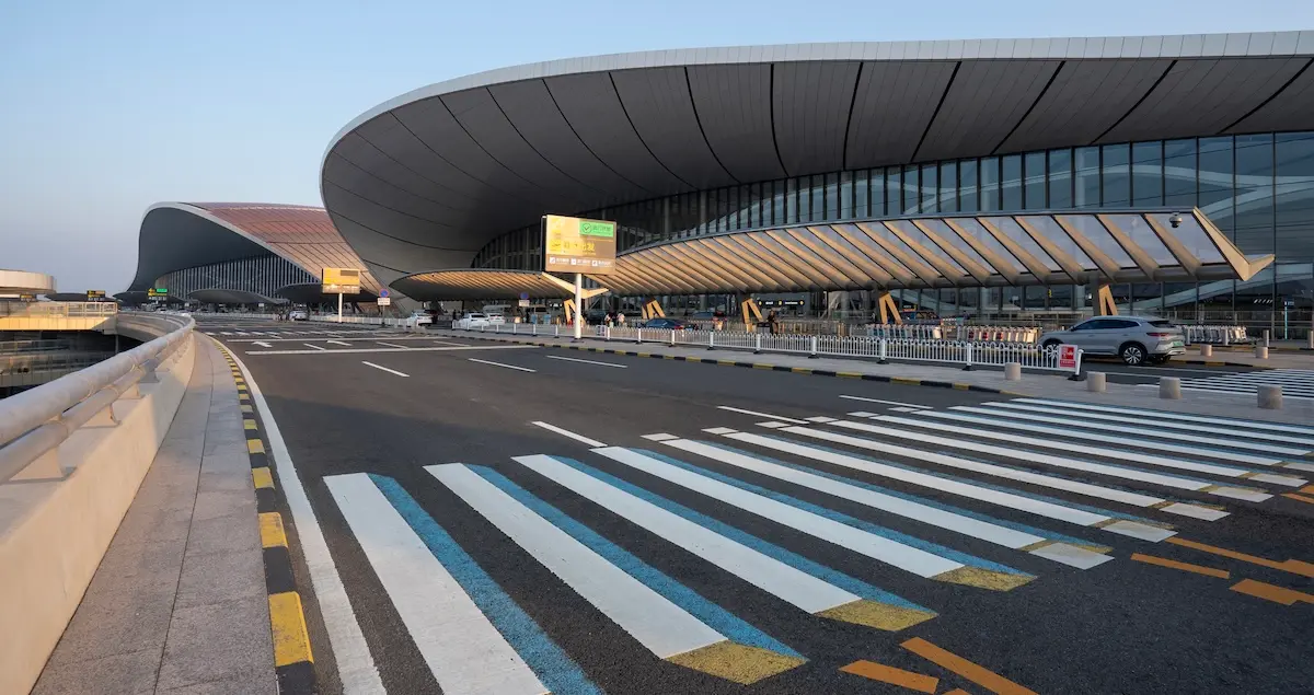 Exterior view of the terminal building at Beijing Daxing International Airport (PKX) showing the road and dropoff area for Departures.