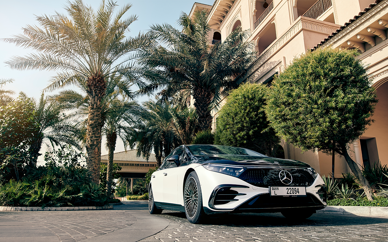 A two-tone Mercedes-Benz EQS parked outside a building with Palm trees out front.